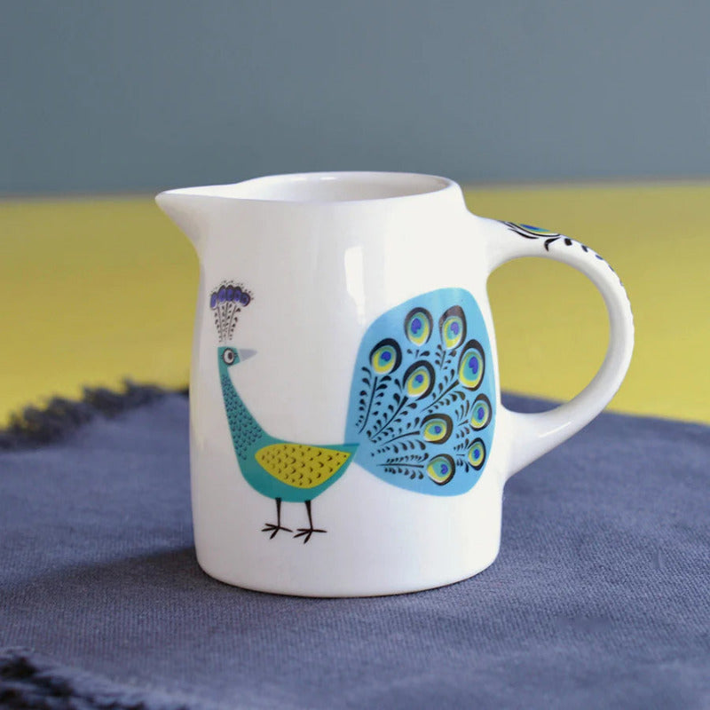 Small white ceramic jug with blue green and yellow folk art style peacock design