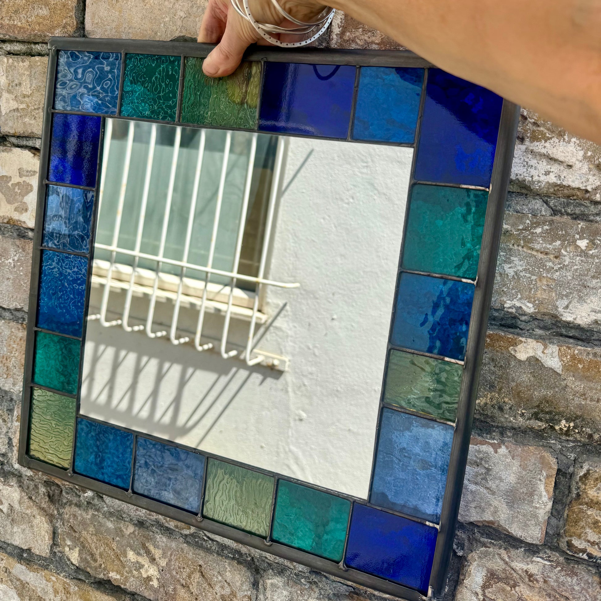 Square stained glass mirror with a 6cm border of greens, blues and aqua colours.
