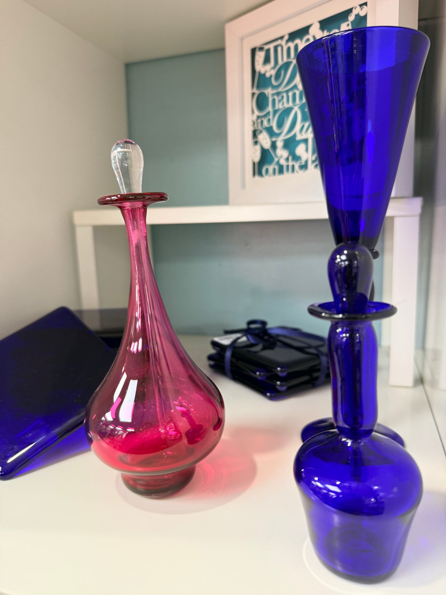 Two glass bottles, one blue and one pink, on a shelf.