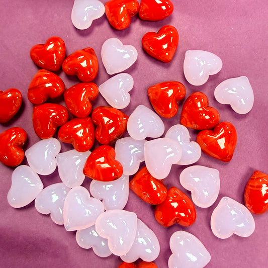 Red and translucent white heart-shaped beads scattered on a dusty purple background.