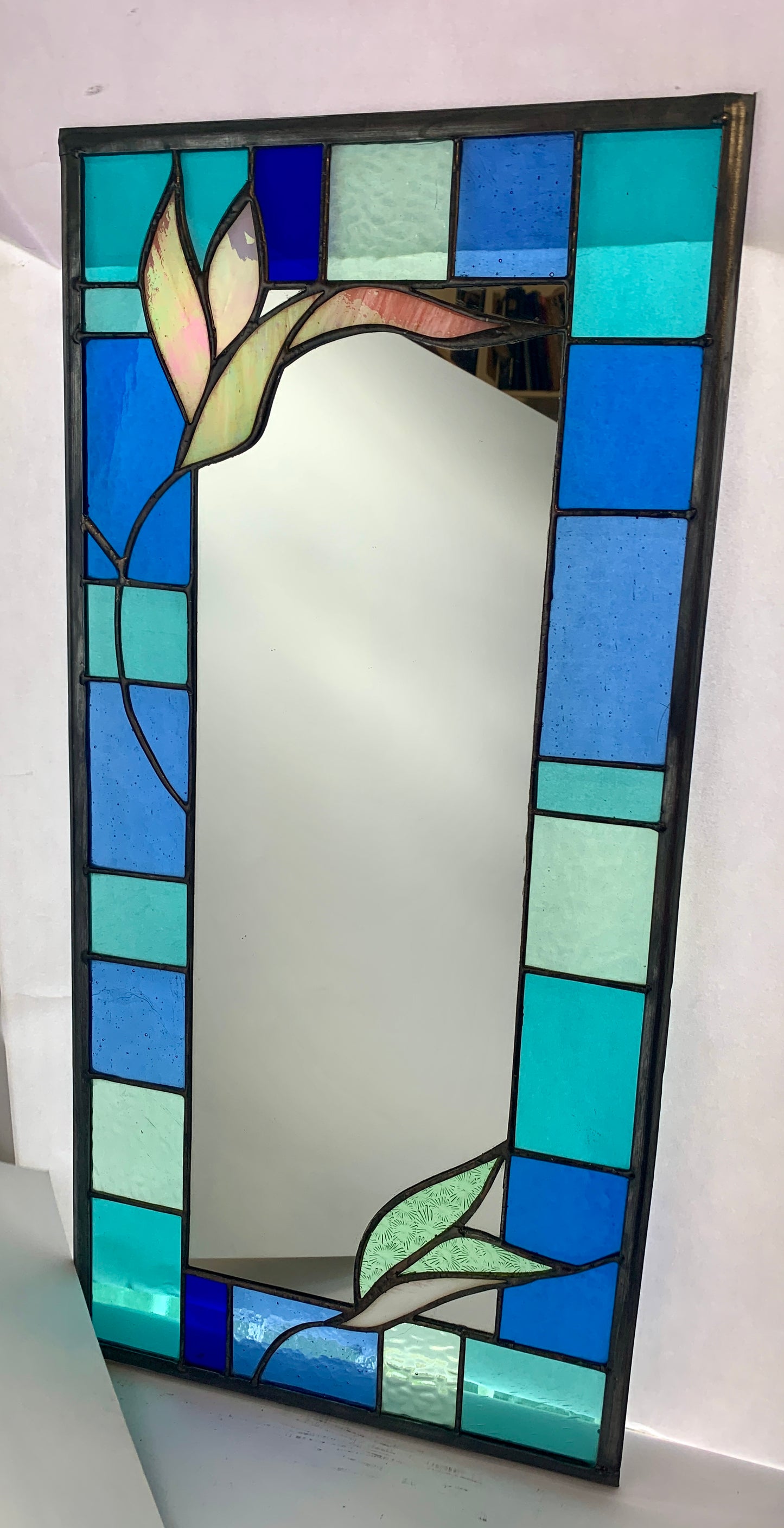 Stained Glass Mirror. Blue and Turquoise border glass; Irridiscent glass floral petals. Made by Dadswell Glass.