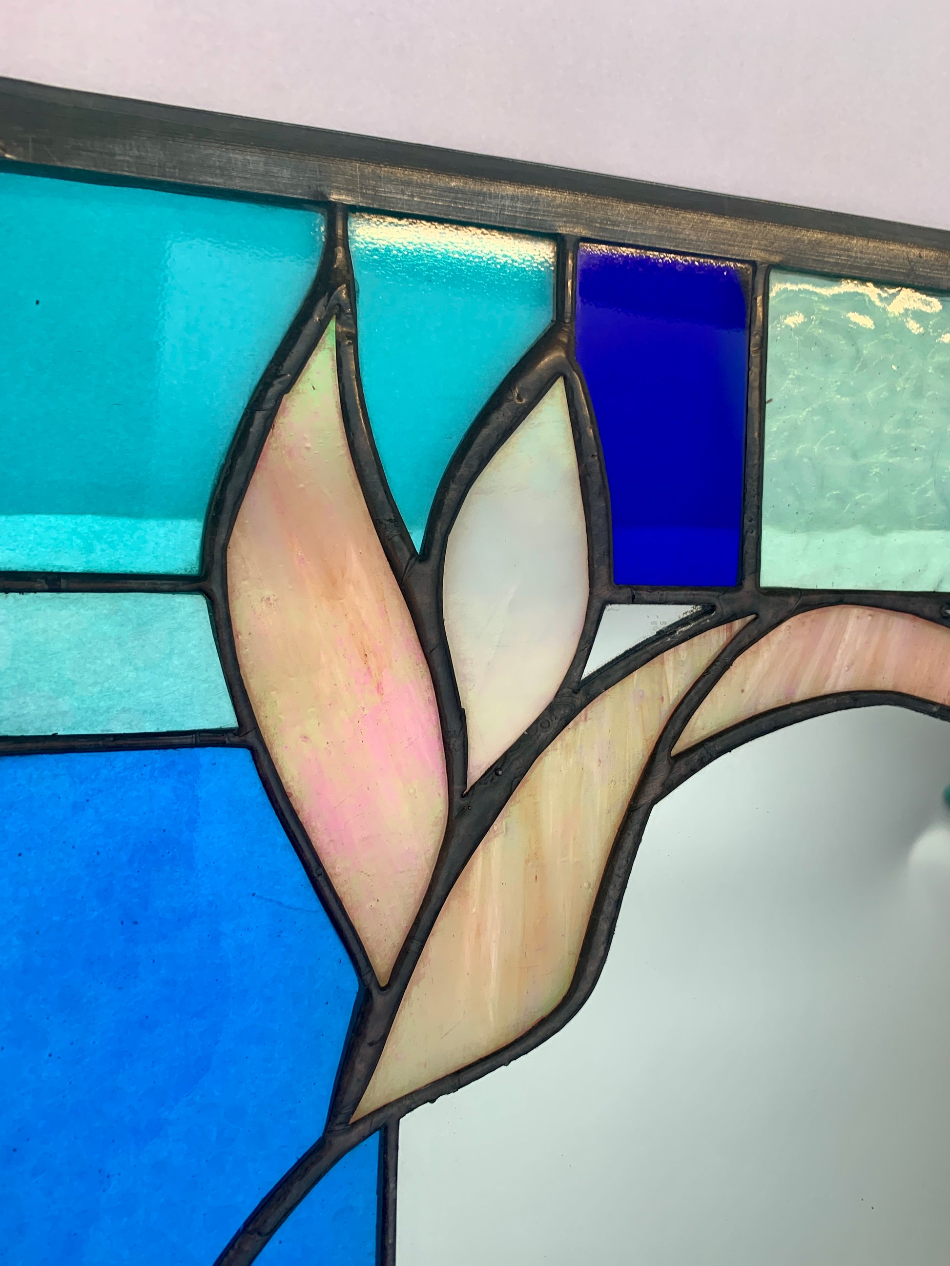Stained Glass Mirror. Blue and Turquoise border glass; Irridiscent glass floral petals. Made by Dadswell Glass.