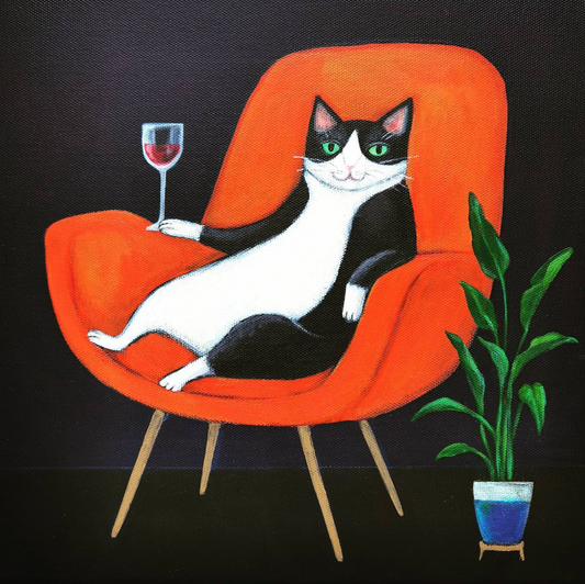 Print of a black and white cat reclining on a red armchair holding a glass of wine