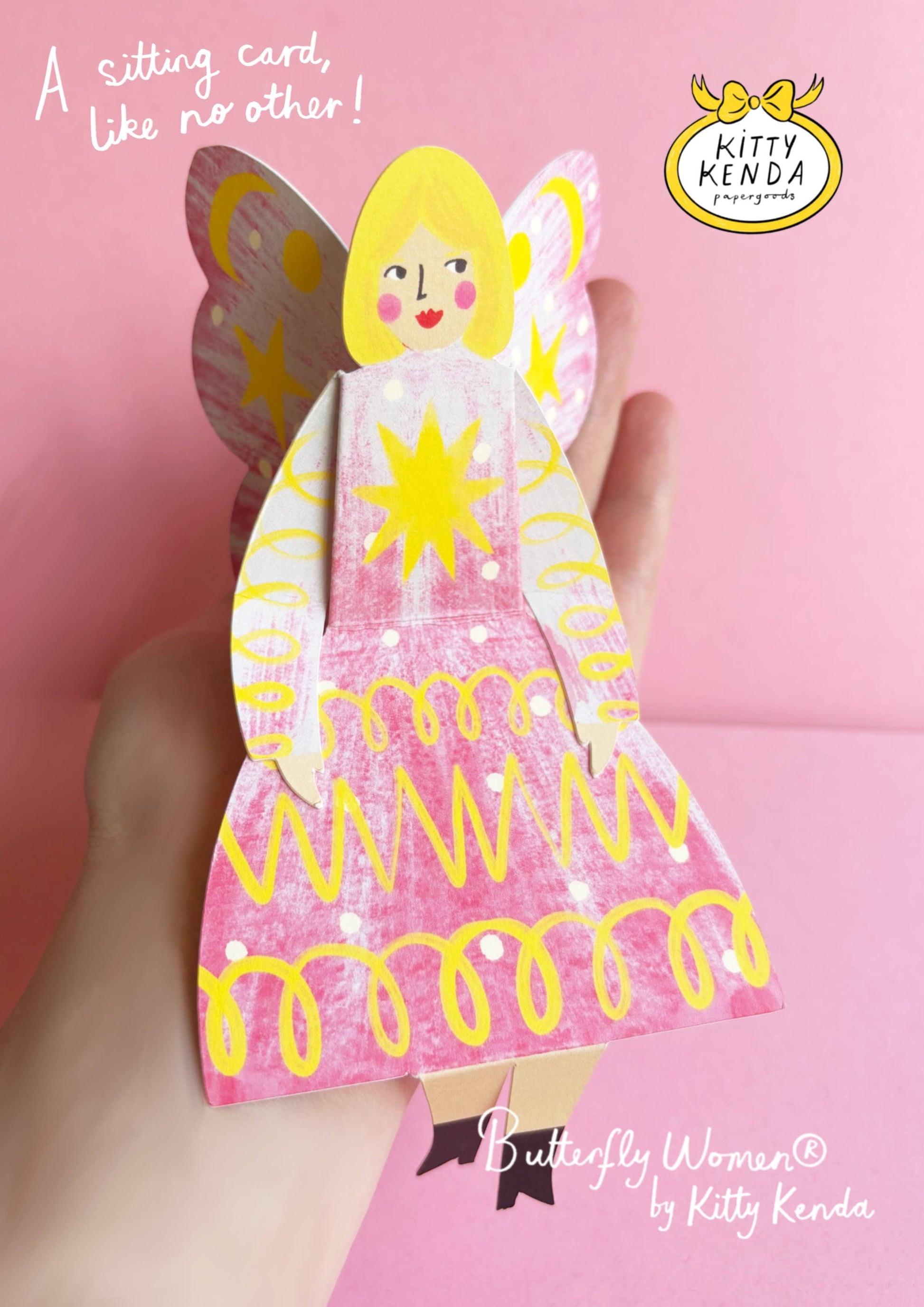 Card shaped like a butterfly woman with pink and yellow design, held against a pink background.