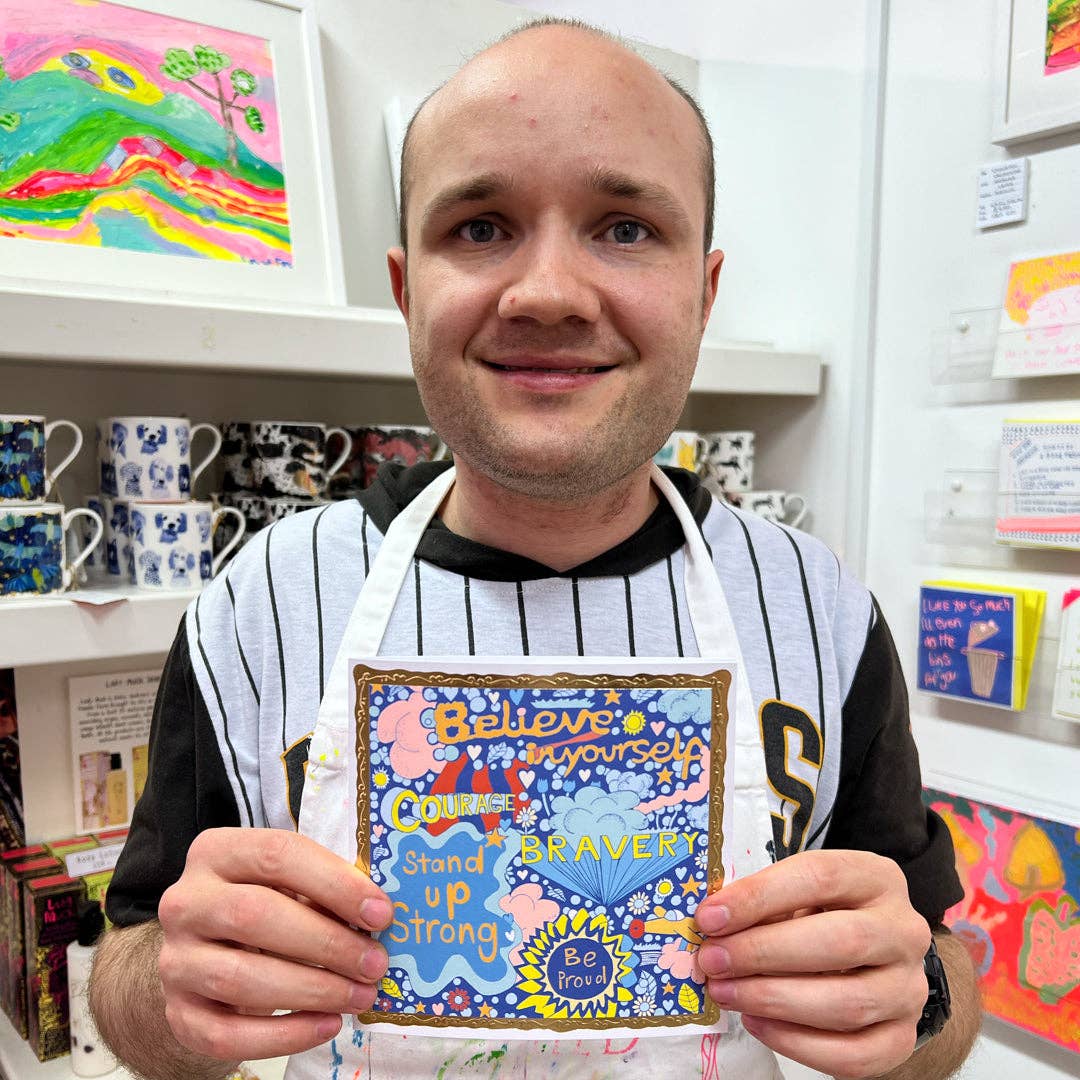 Man holding a colorful card with motivational text in an art store.