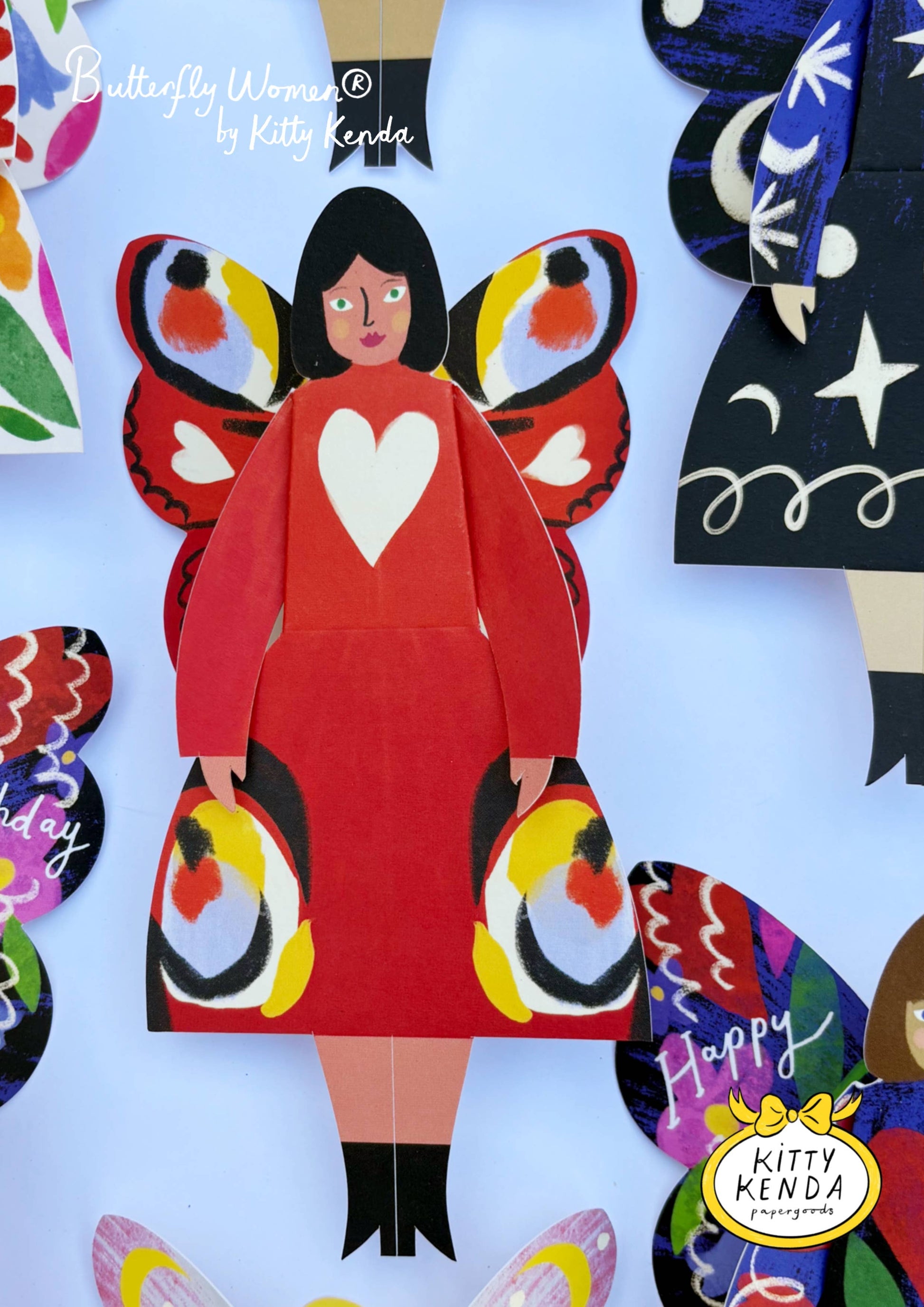 Colorful paper cutout of a woman with butterfly wings and a heart on her dress, featuring the brand 'Kitty Kenda'.