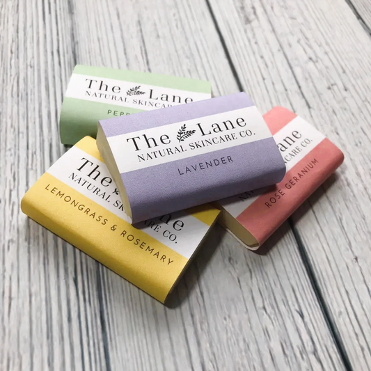 Five bars of soap from The Lane Natural Skincare Co. on a wooden surface.