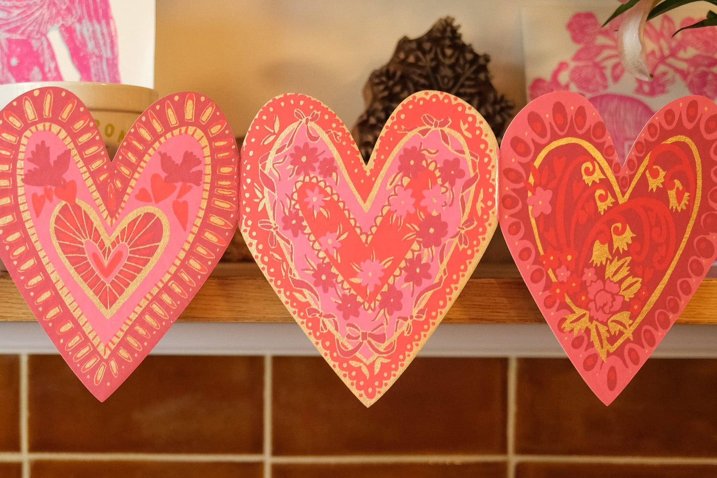 Three heart-shaped decorative items with floral patterns on a shelf.