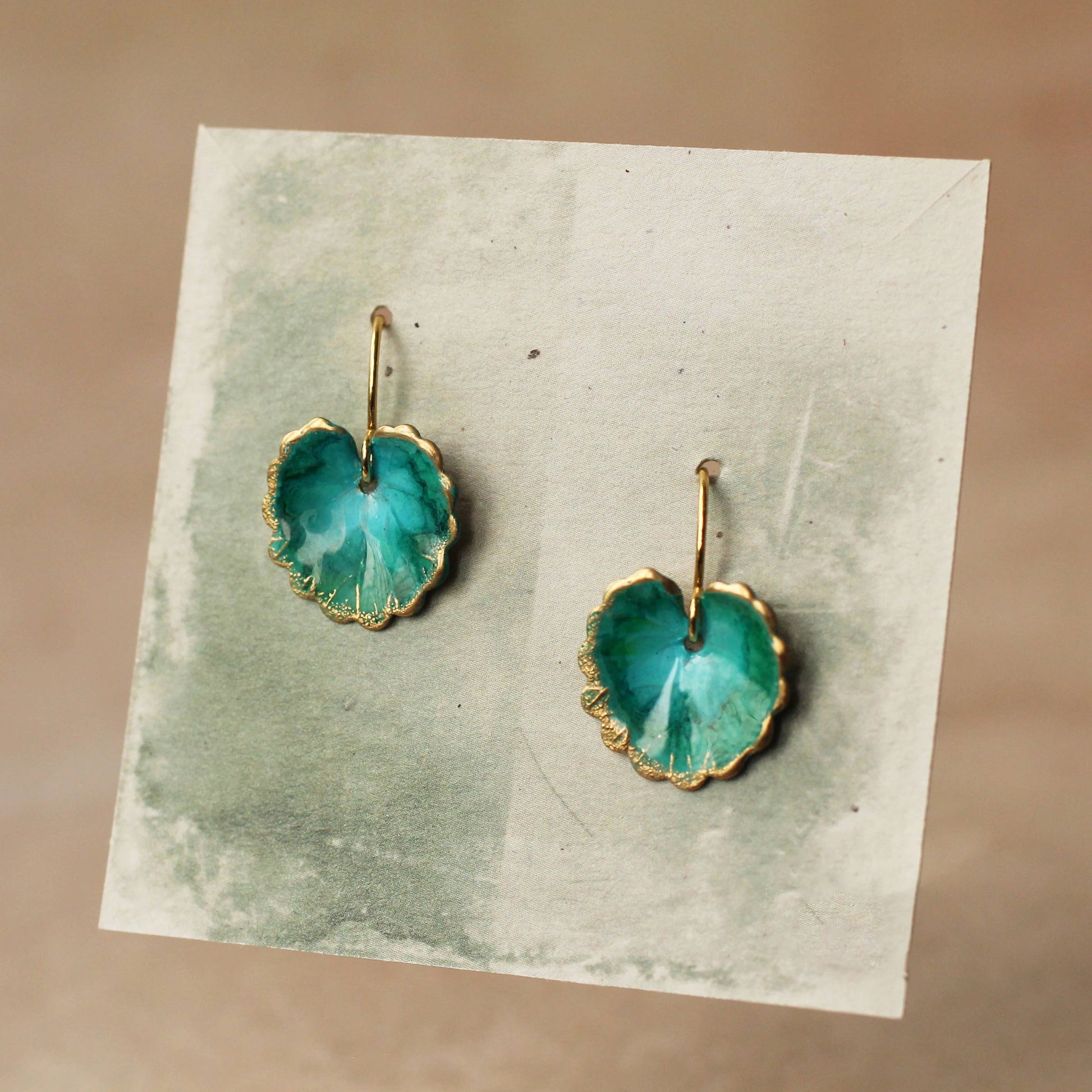 Pair of green earrings on a textured card with a beige background