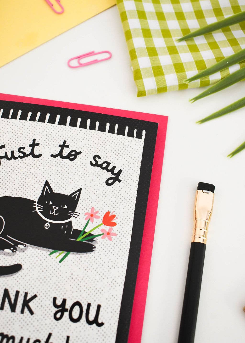 Greeting card with a cat illustration and text on a white surface with a pen and paper clips.