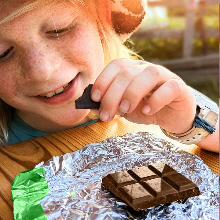 Child eating a chocolate bar with a piece of foil on a wooden table