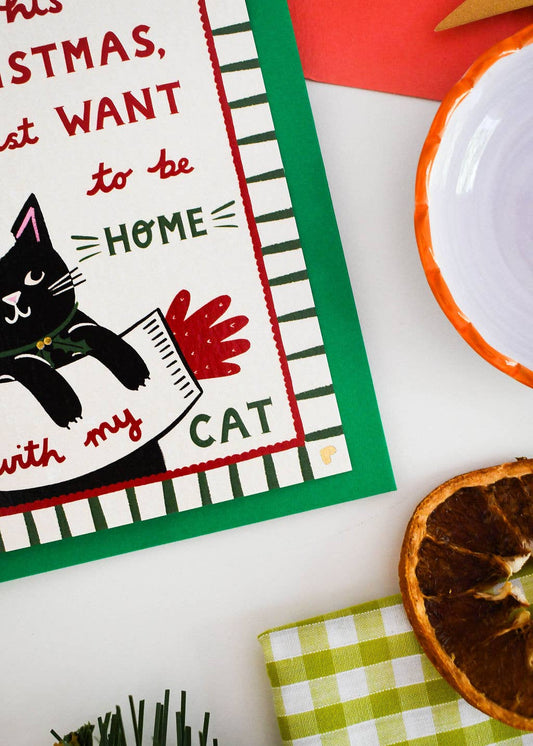 A festive Christmas-themed tea towel laid flat on a white surface, styled with a dried orange slice, a green-and-white checkered napkin, and a white bowl with an orange rim.