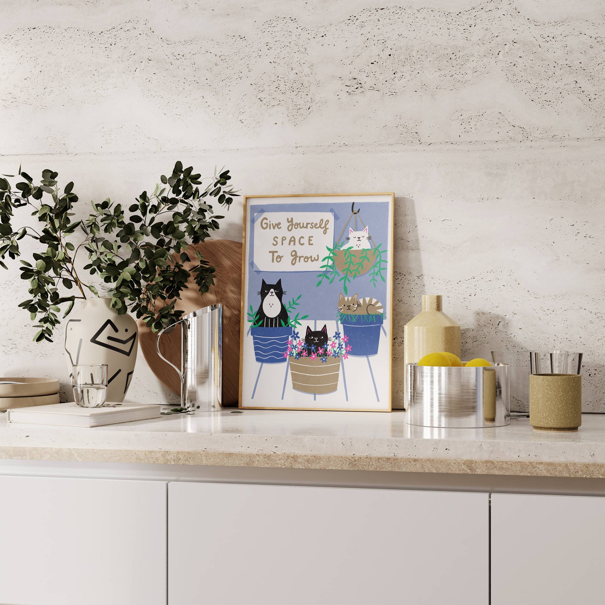 Decorative elements on a kitchen counter with a framed print and plants.