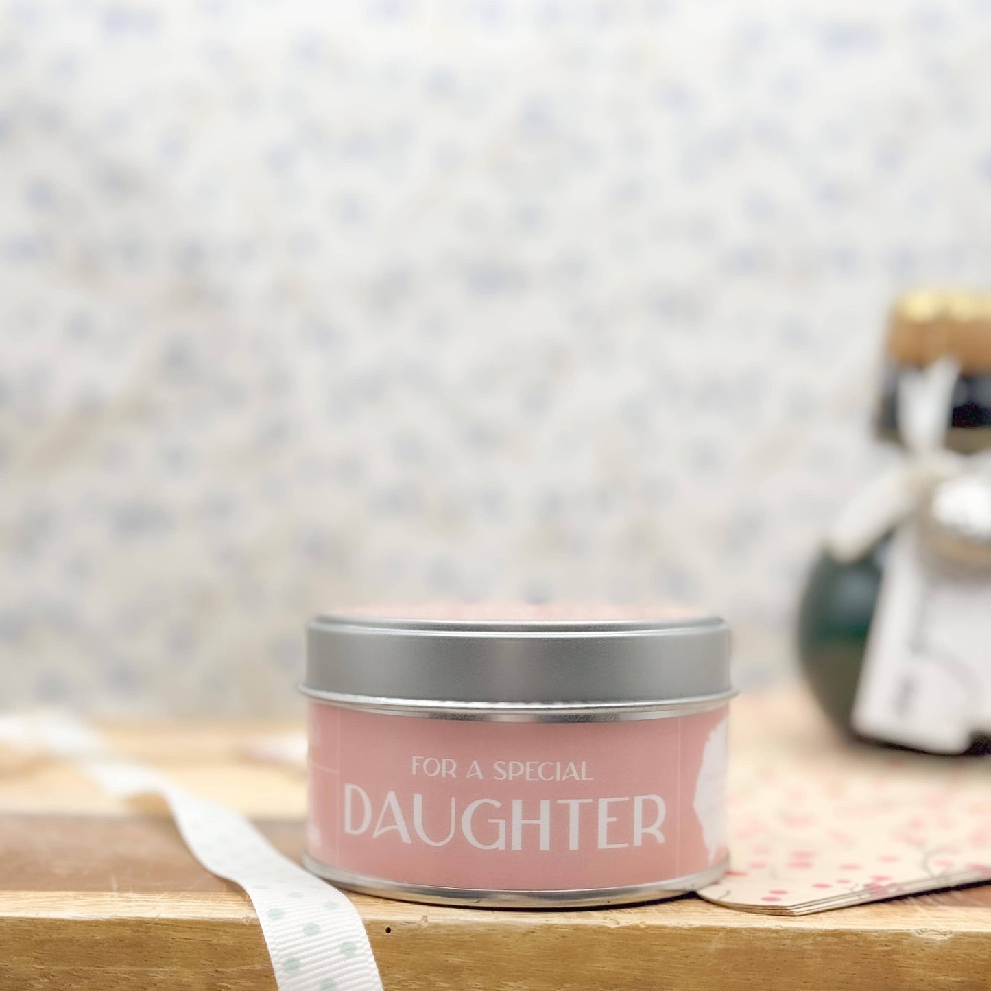 Candle in a tin labeled 'For a Special Daughter' on a wooden surface with a blurred background.