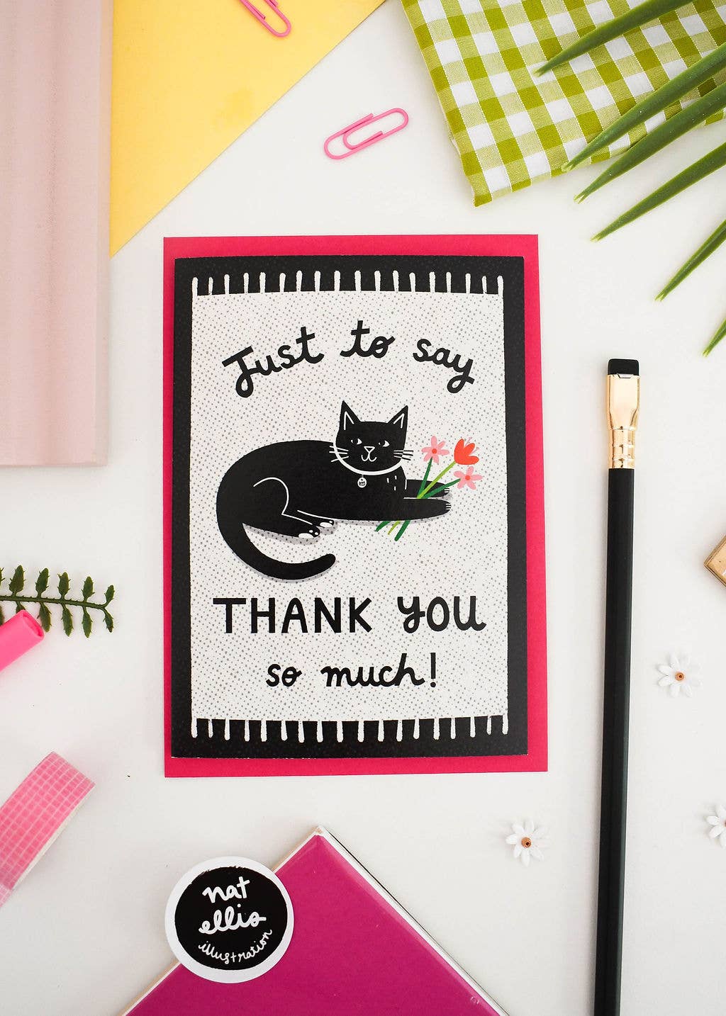 Greeting card with a black cat illustration and text on a white background with stationery items.