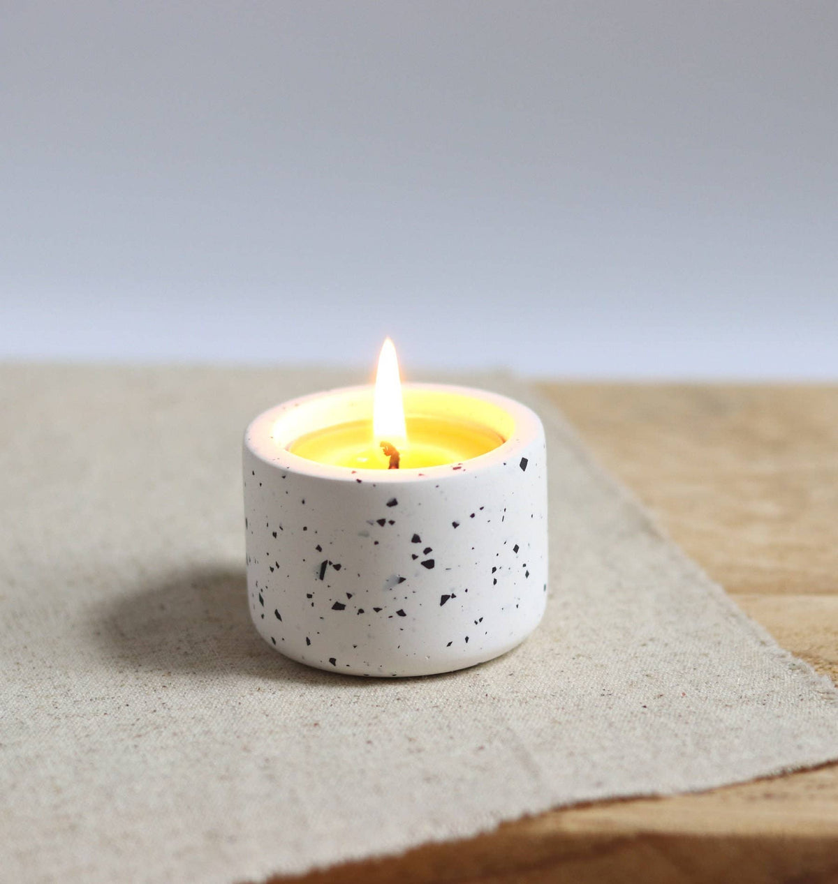 Speckled white candle holder with a lit candle on a textured surface