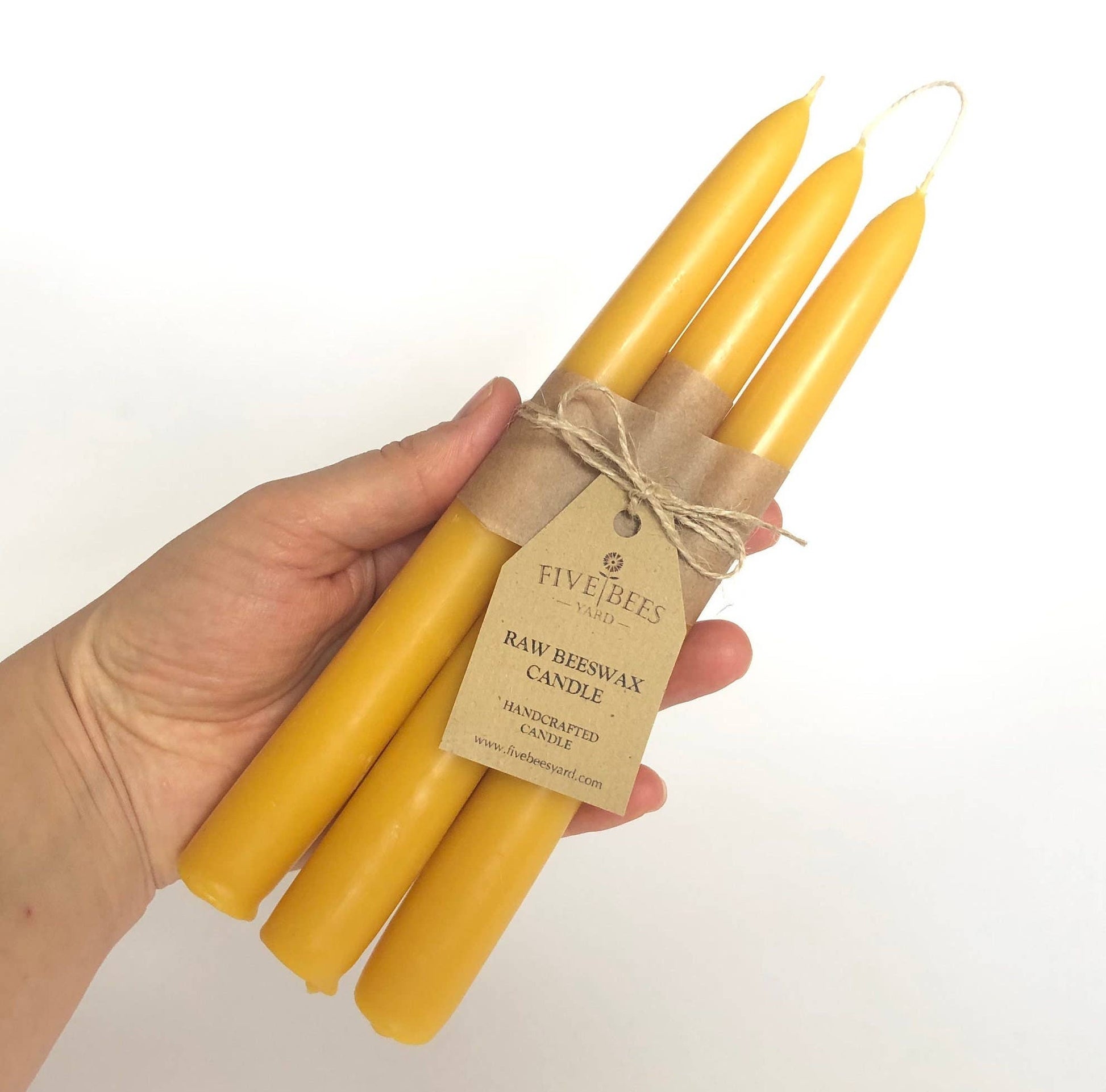 Hand holding four yellow candles tied with twine, branded 'Five Bees London'.