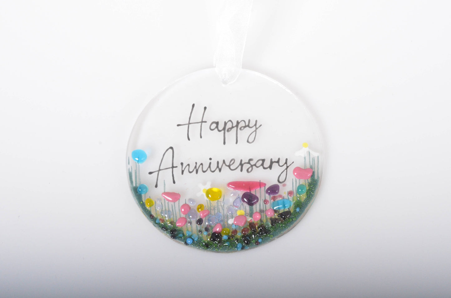 Round decorative item with 'Happy Anniversary' text and colorful flowers on a white background