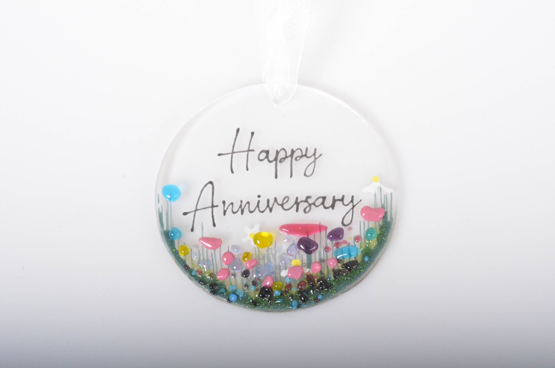 Round decorative item with 'Happy Anniversary' text and colorful flowers on a white background