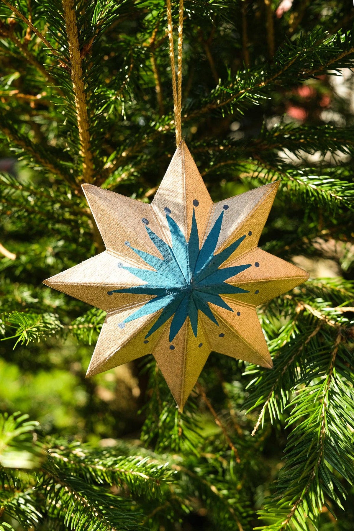 Star-shaped Christmas ornament with blue center hanging on a tree