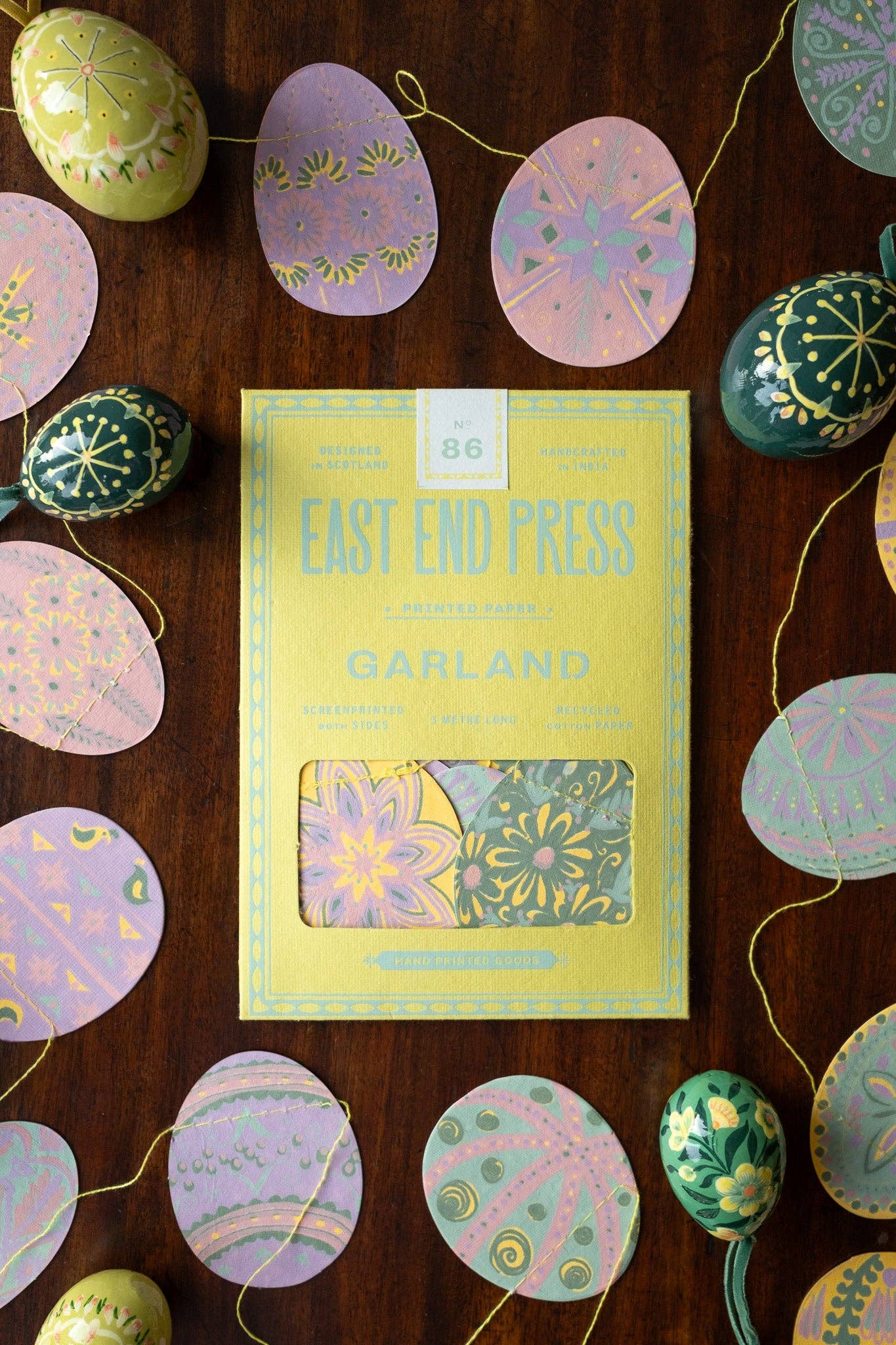 Book titled 'Garland' by East End Press surrounded by decorative Easter eggs on a wooden surface.