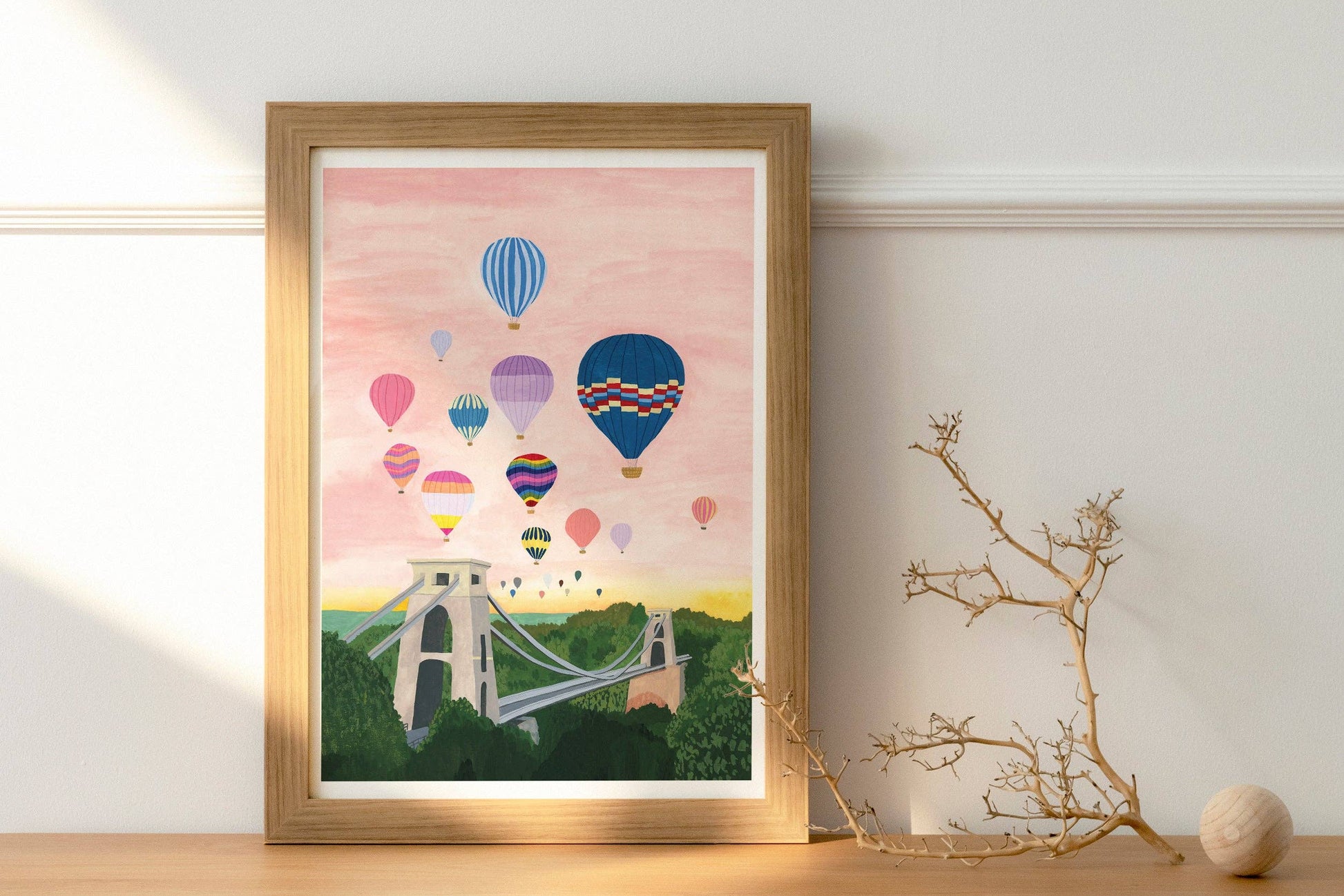 Framed artwork of hot air balloons over a bridge on a pink background