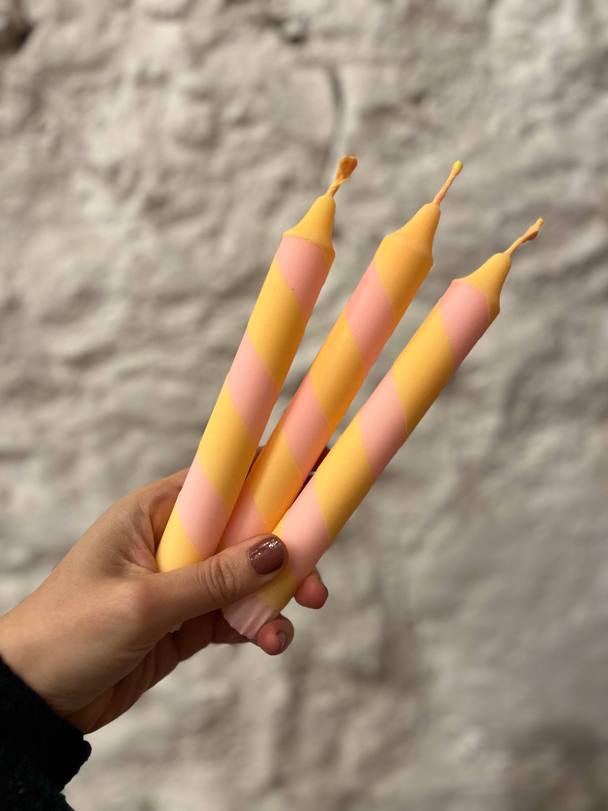 Hand holding three gradient candles against a textured gray background