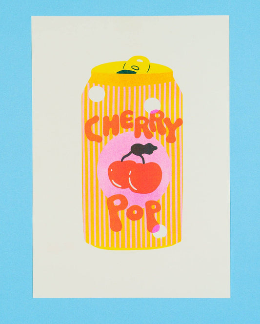 A square art print featuring a stylized yellow can graphic with vertical stripes, a pink circle, two red cherries, and the words 'CHERRY POP' in orange-red lettering, centered on an off-white sheet against a light blue background.