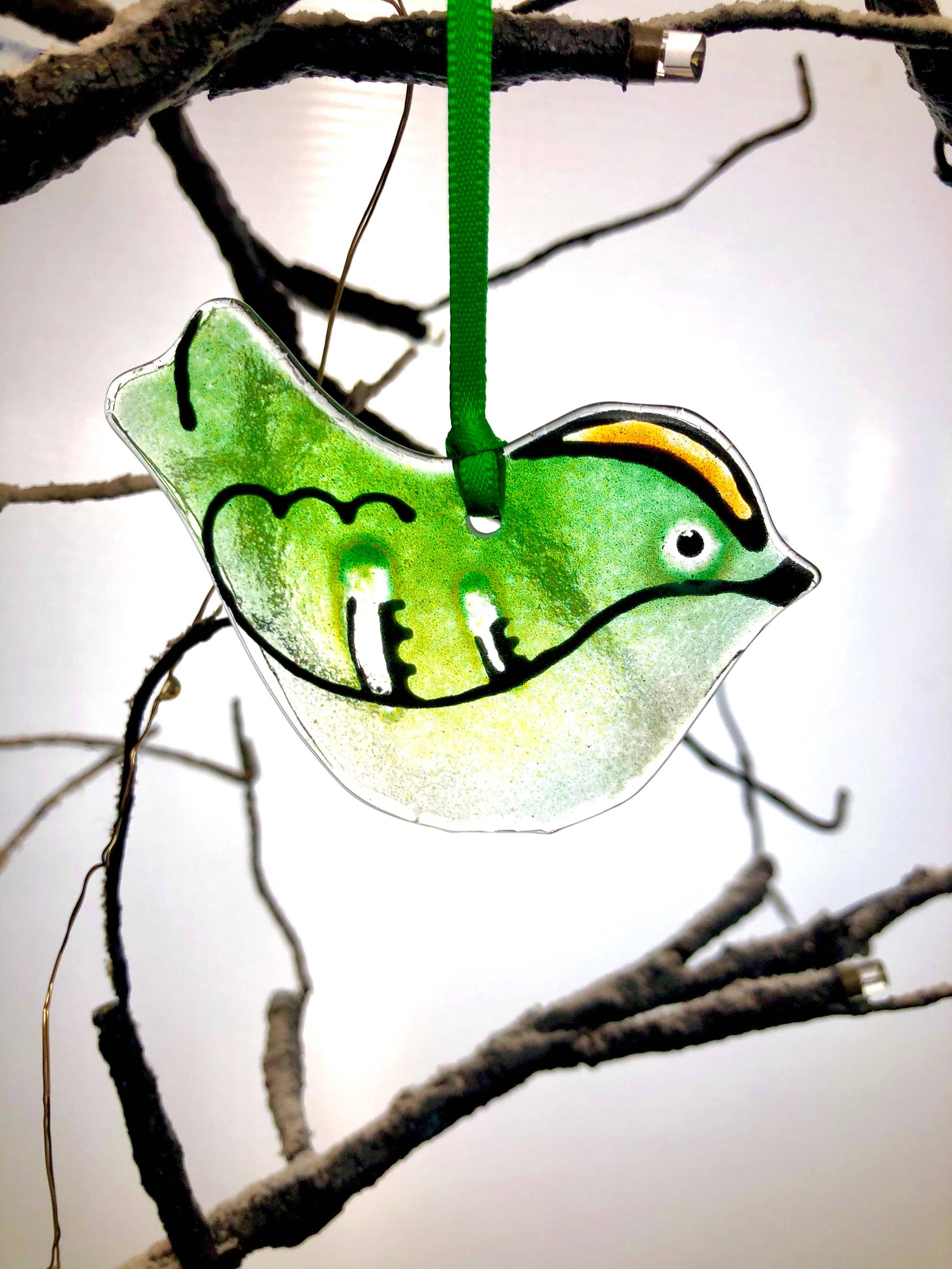 Green glass bird ornament hanging on a branch against a light background