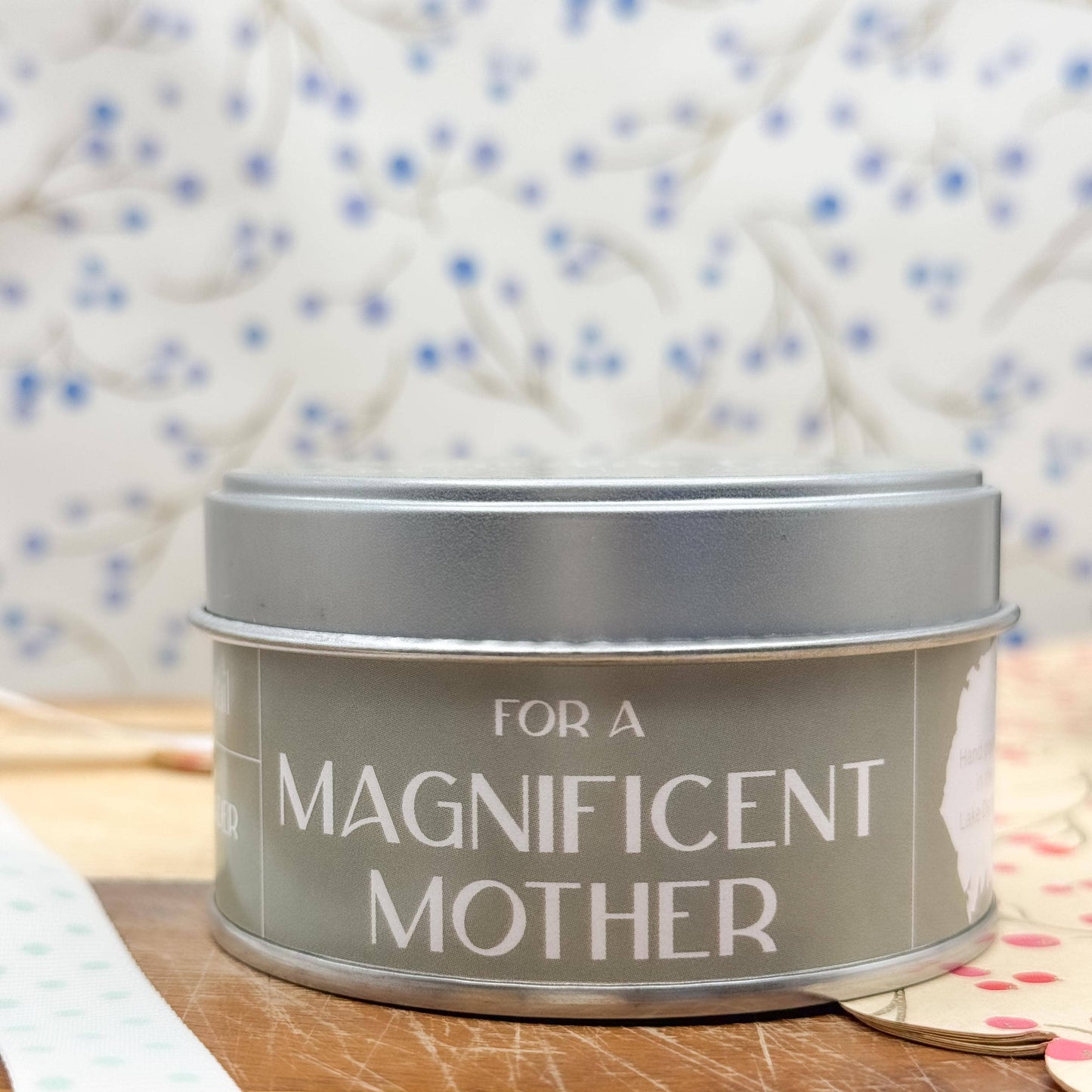 Silver tin with 'For a Magnificent Mother' text on a wooden surface with a patterned fabric background.