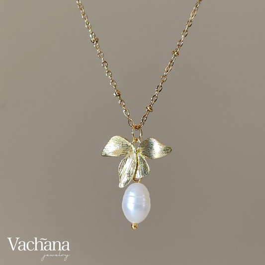 Gold necklace with leaf design and pearl pendant on a brown background, featuring the brand 'Vachana'.