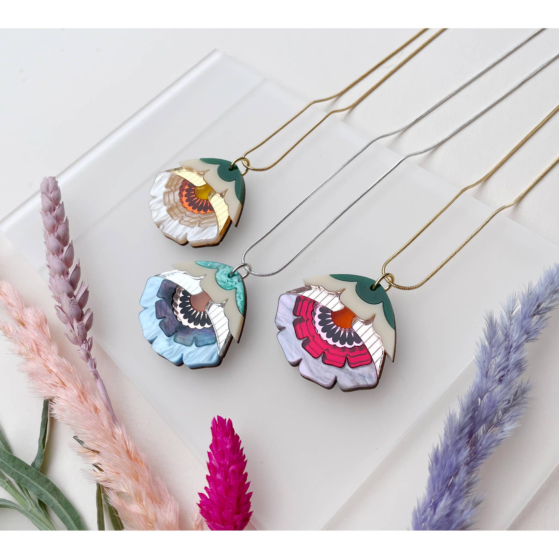 Colorful floral pendant necklaces on a white surface with dried flowers.