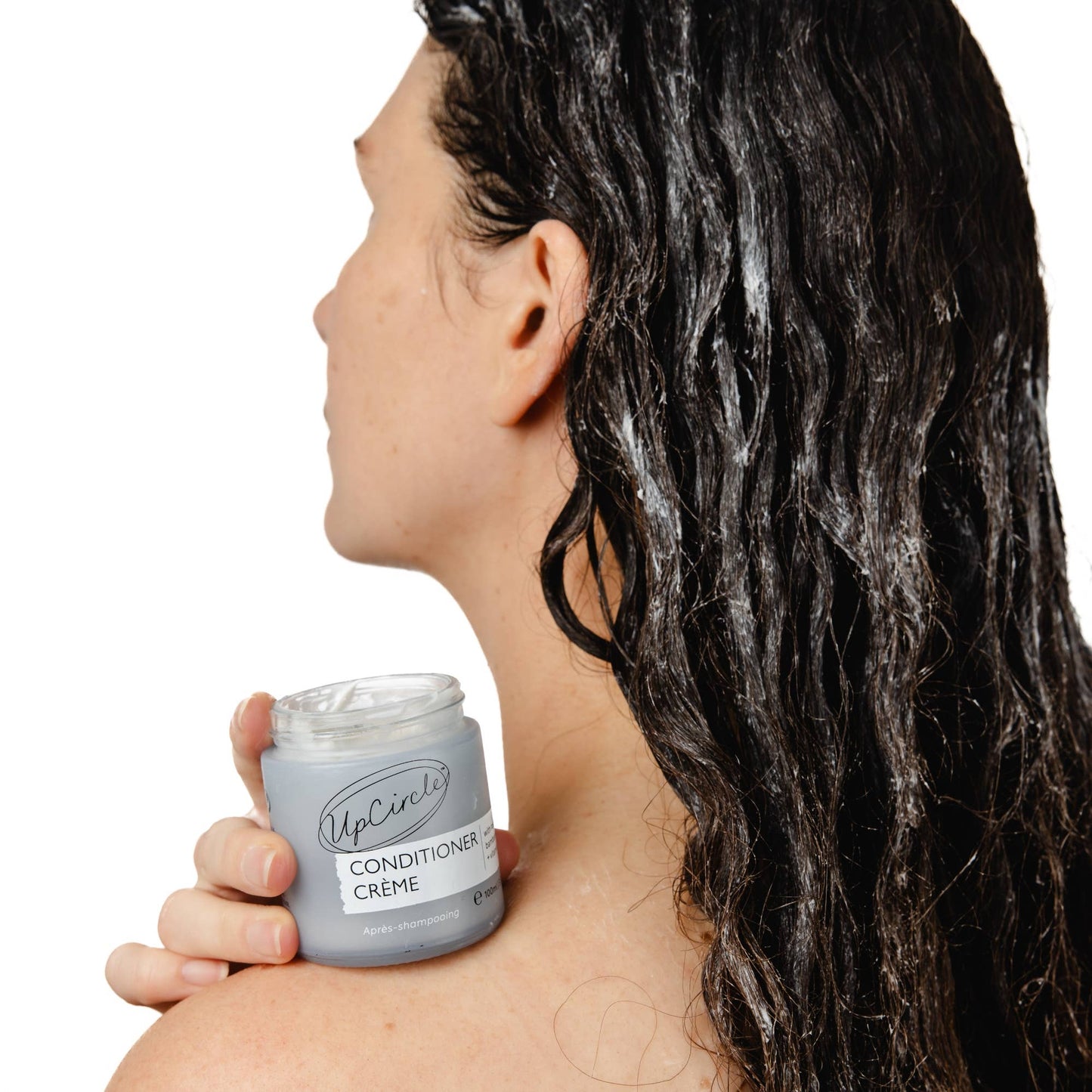 Person holding a jar of UpCircle Conditioner Creme with wet hair.