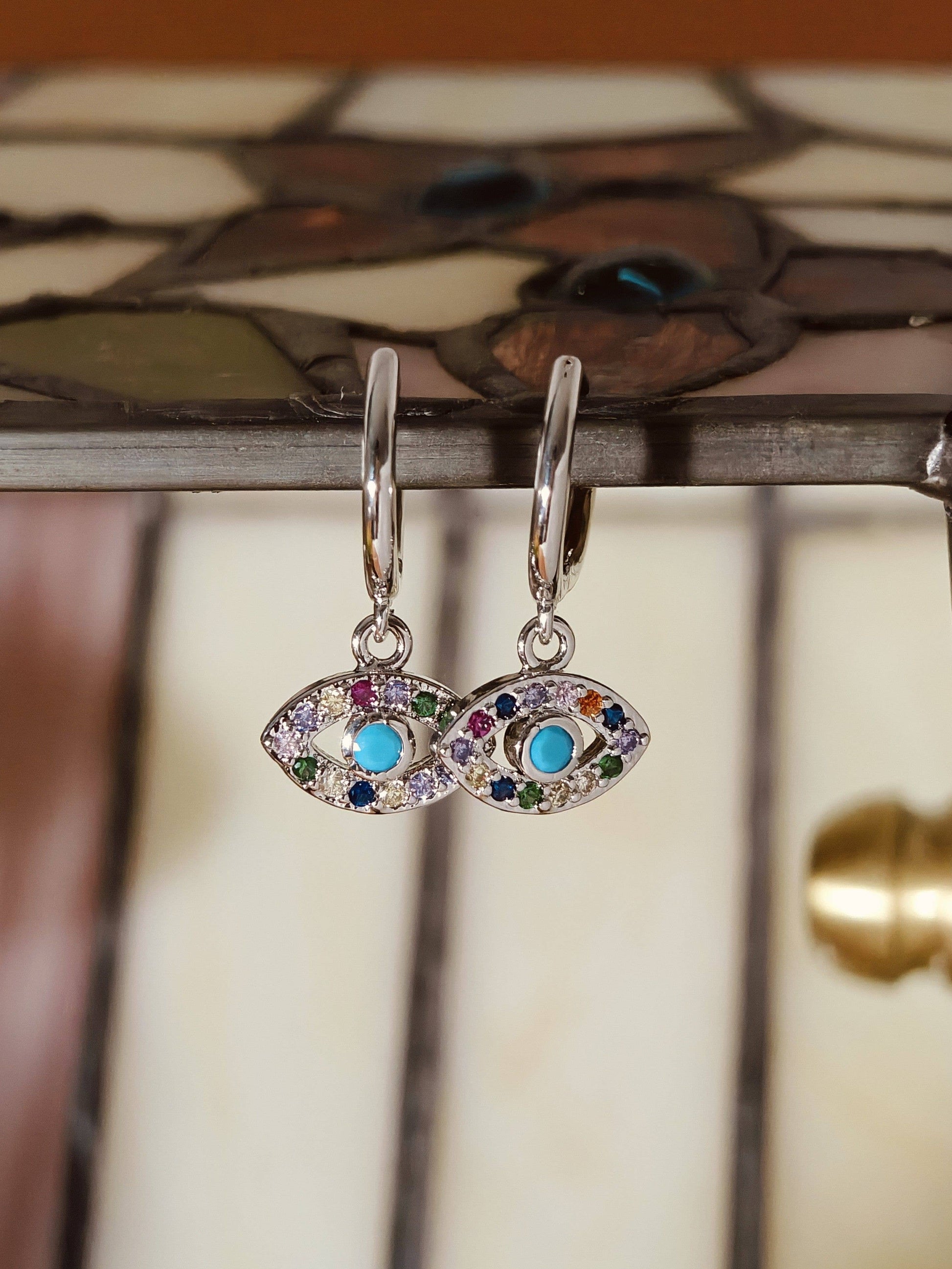Pair of eye-shaped earrings with colorful gemstones on a decorative background