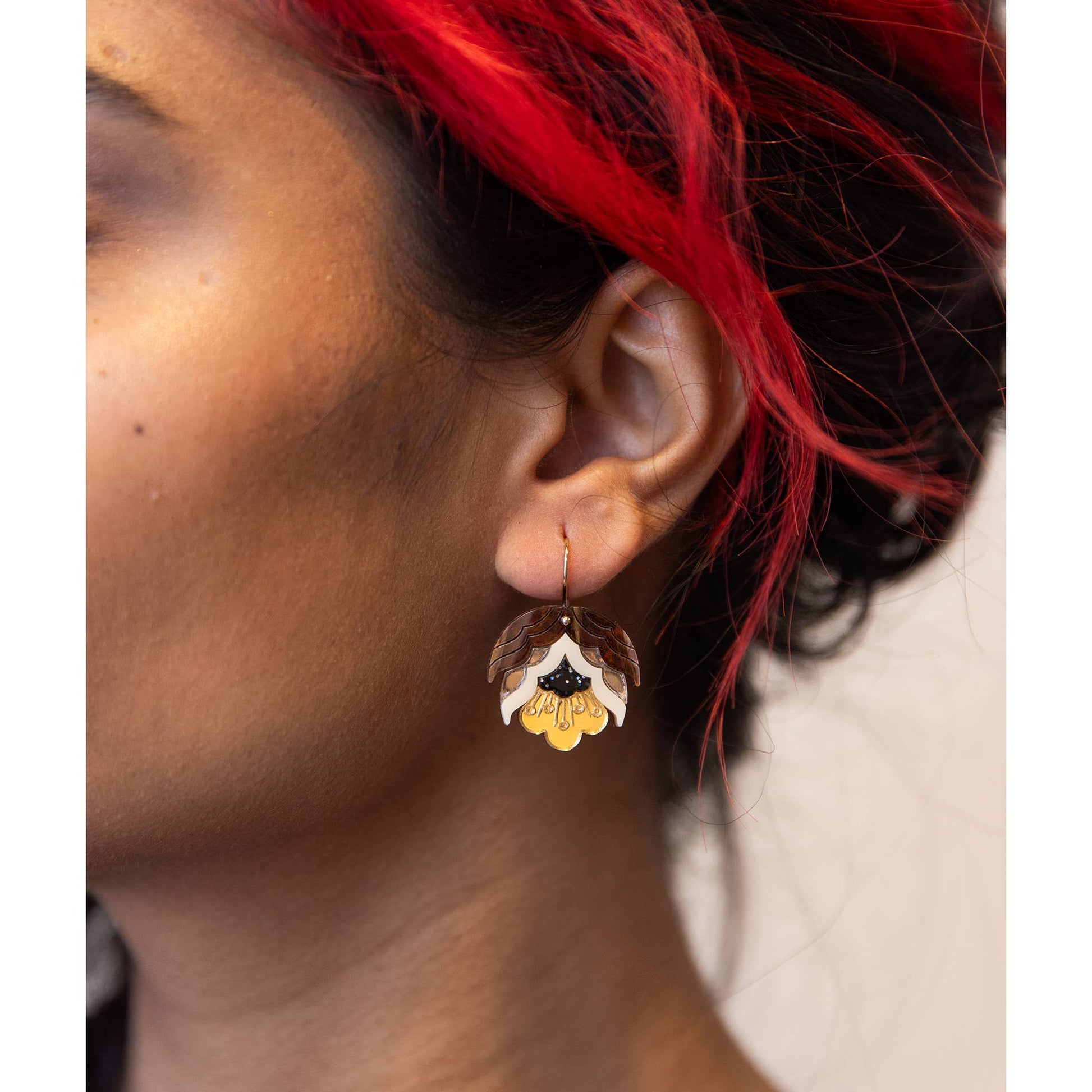 A close-up of a person's ear wearing a dangling flower-shaped earring with brown, white, and yellow petals.