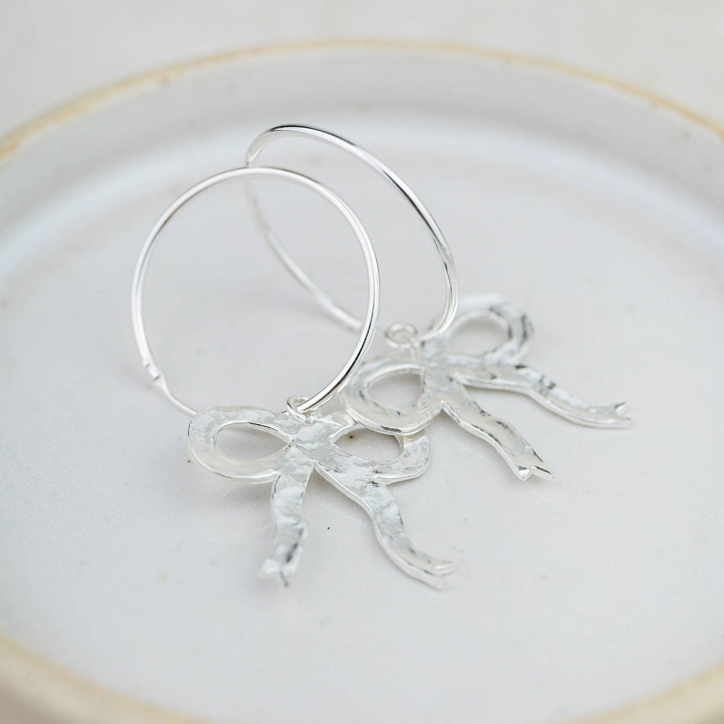 Silver hoop earrings with leaf-like designs on a white plate