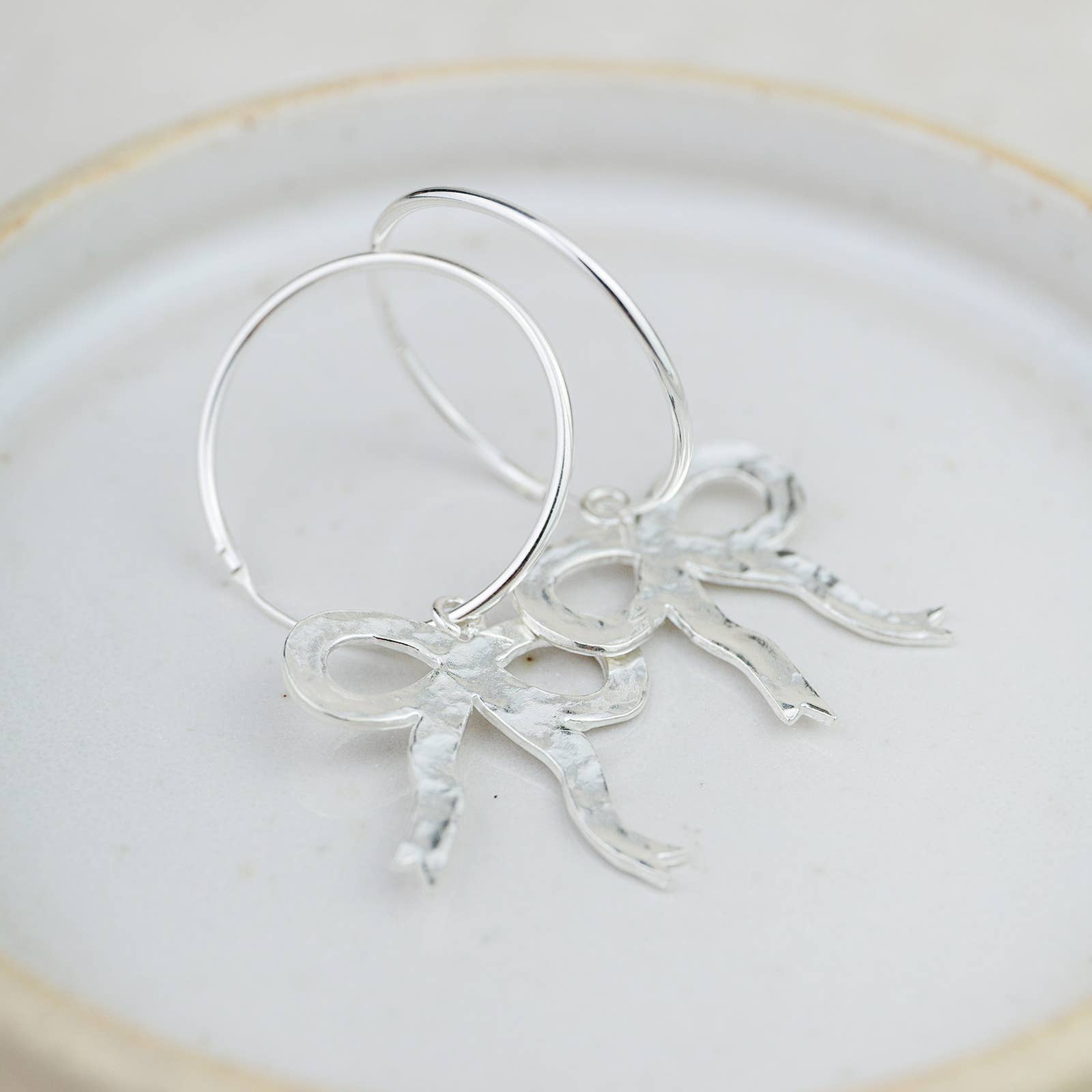 Silver hoop earrings with leaf-like designs on a white plate
