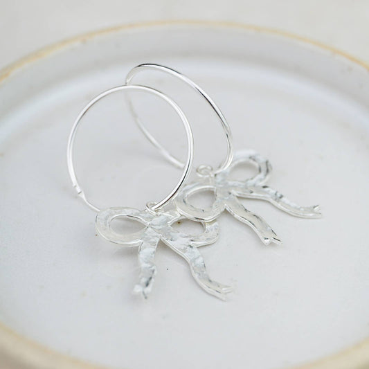 Silver hoop earrings with leaf-like designs on a white plate