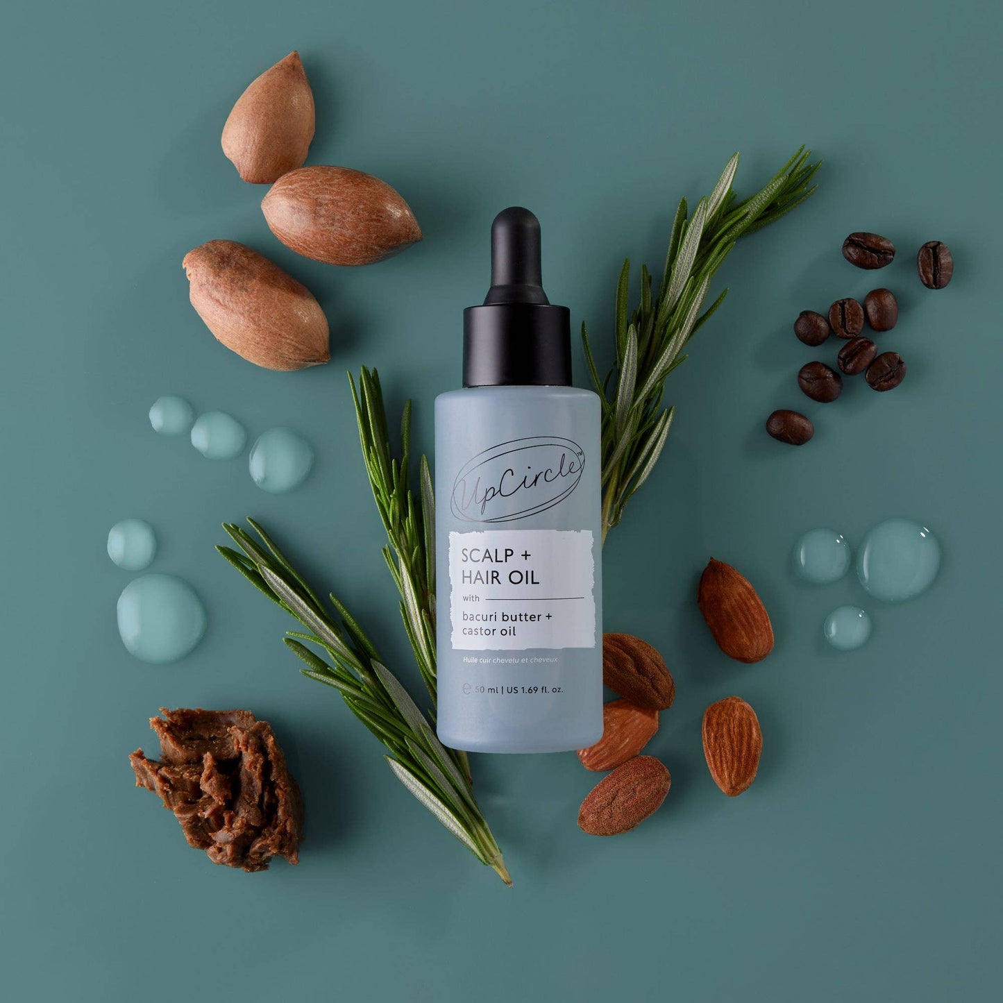 Bottle of scalp and hair oil with almonds, coffee beans, and rosemary on a teal background