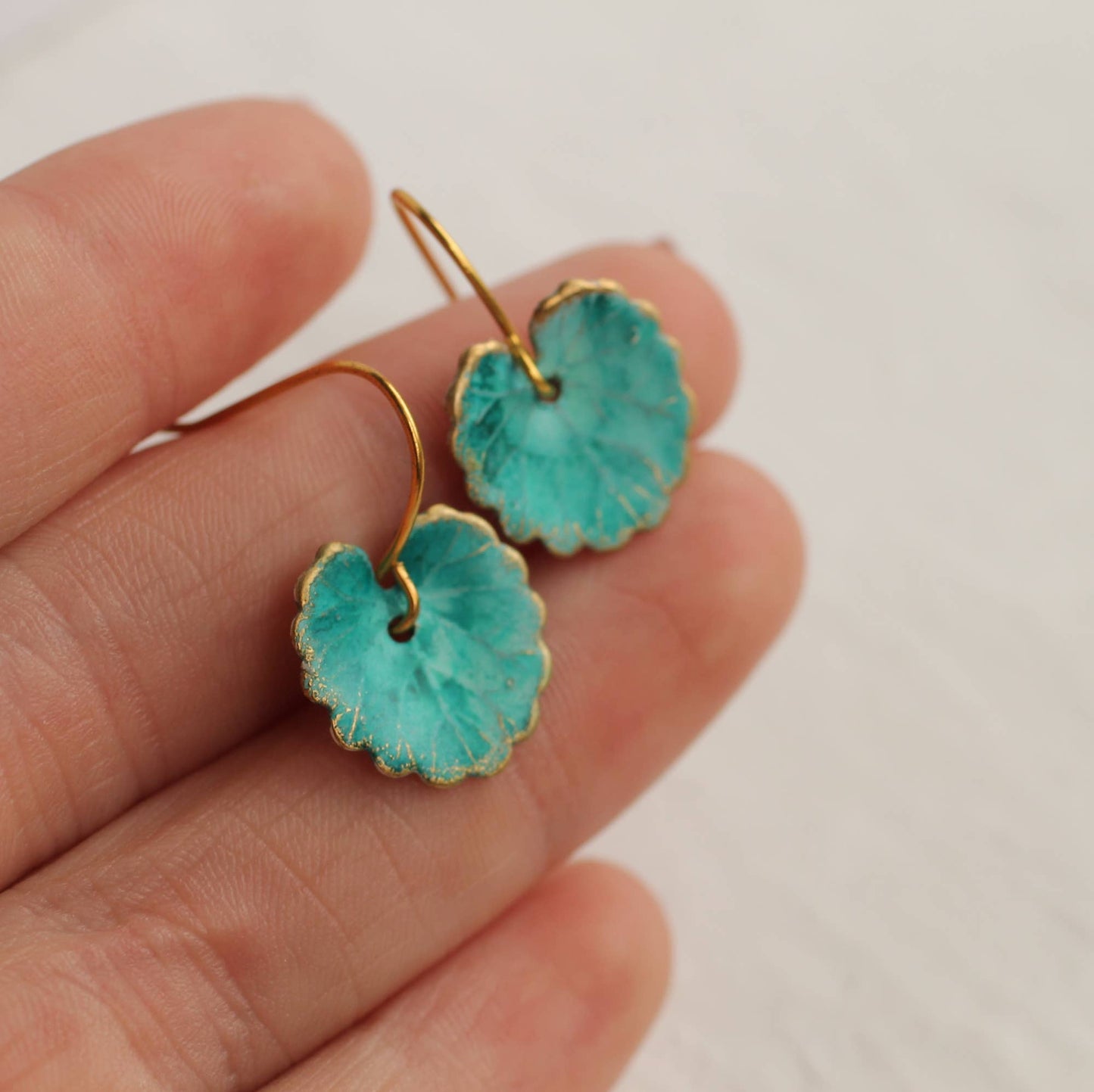 Turquoise earrings with gold accents held between fingers against a neutral background