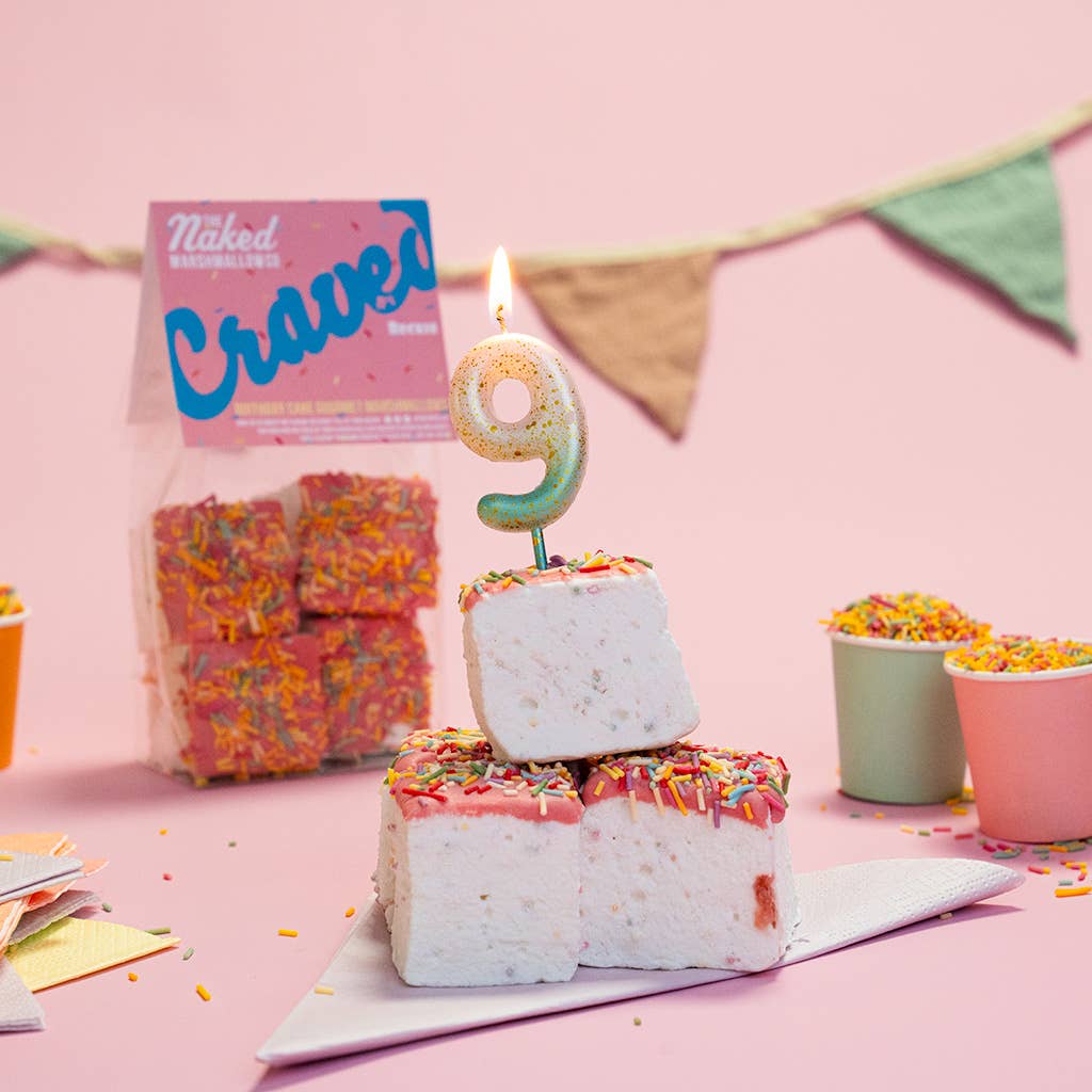 Stack of colorful marshmallow bars with a number 9 candle on a pink background, featuring 'Naked Crave' packaging.