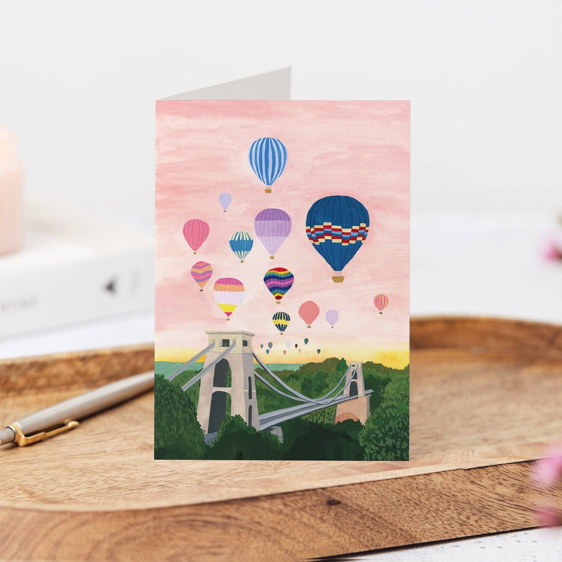 Greeting card with hot air balloons and a bridge illustration on a wooden surface.