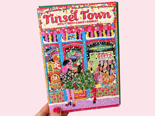 Colorful magazine cover titled 'Tinseltown' held by a hand on a pink background