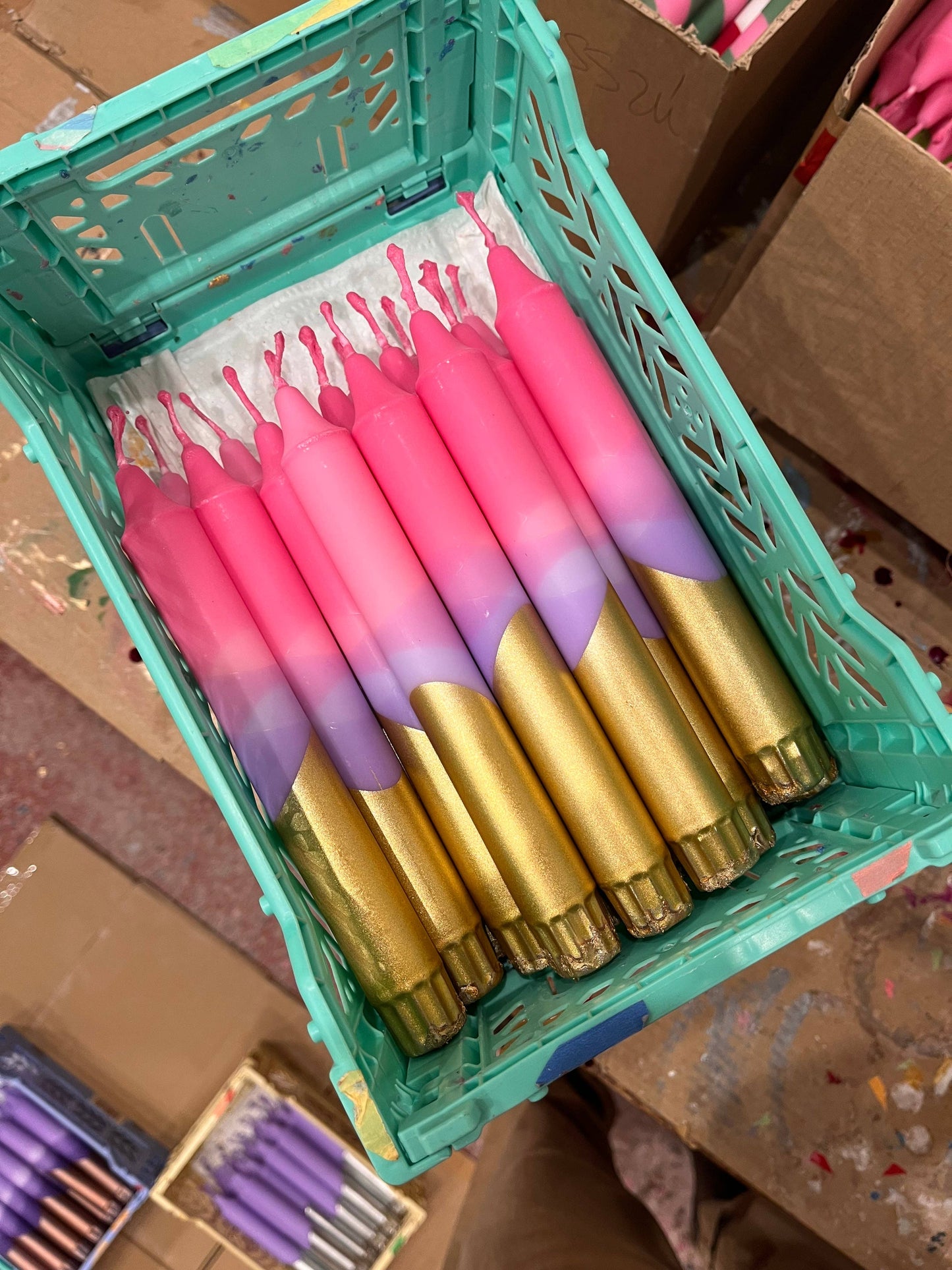 Gradient candles in pink and gold in a green crate on a cardboard background