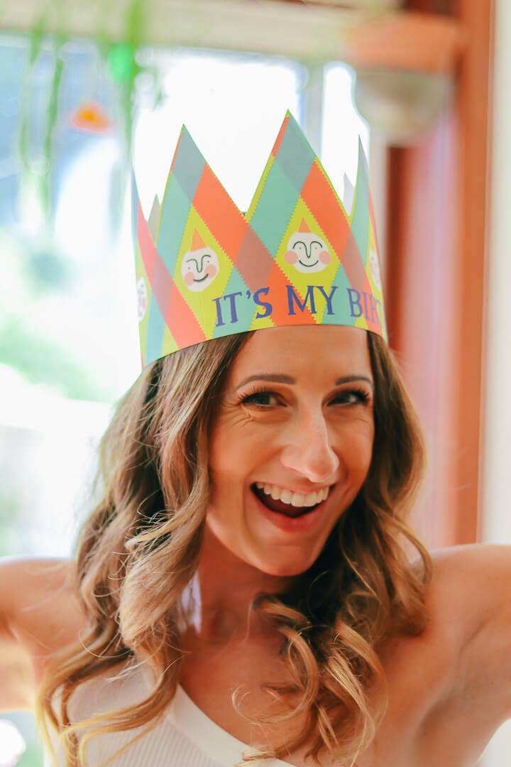Woman wearing a colorful 'It's My Birthday' party hat indoors.