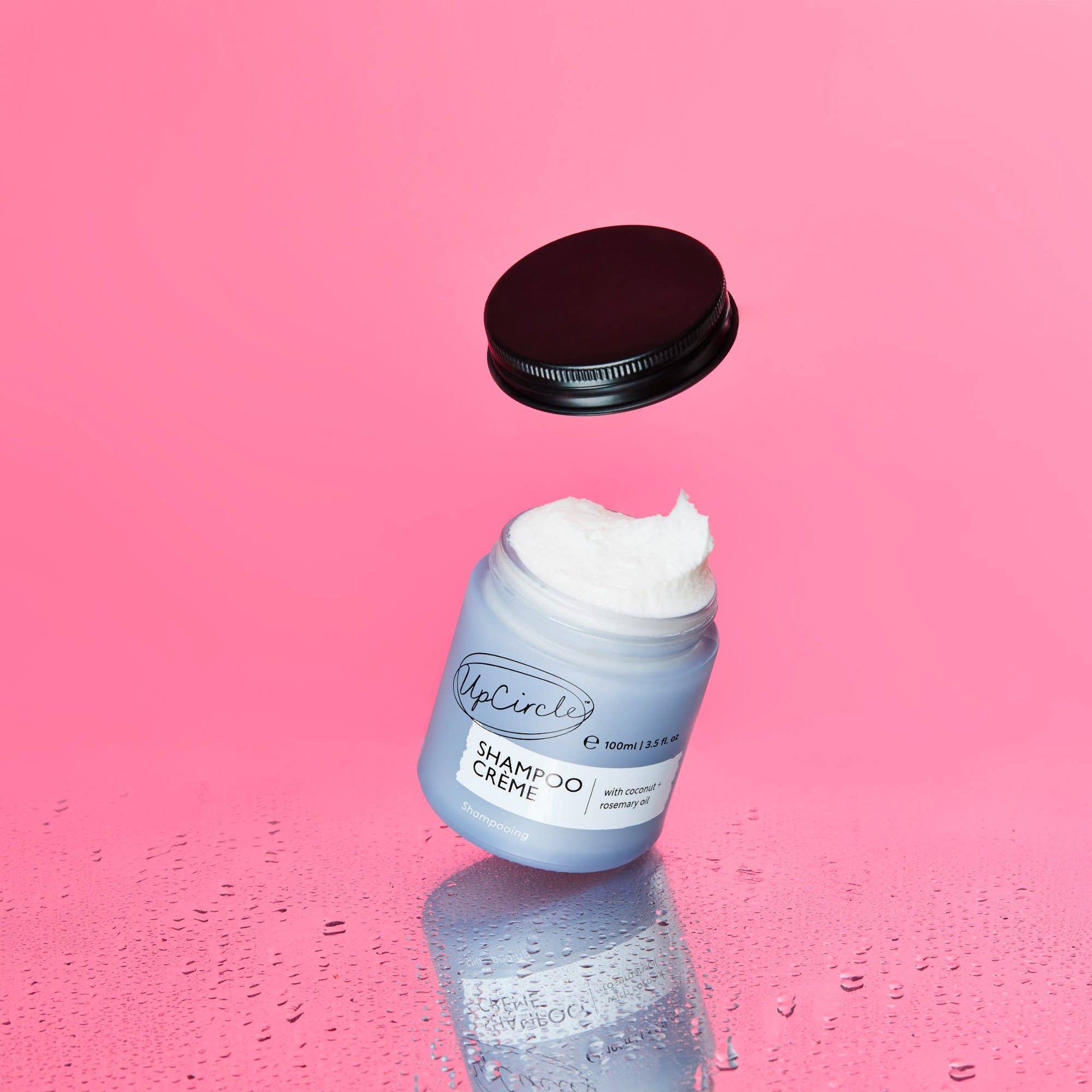 Blue jar of shampoo crème with a black lid on a pink background