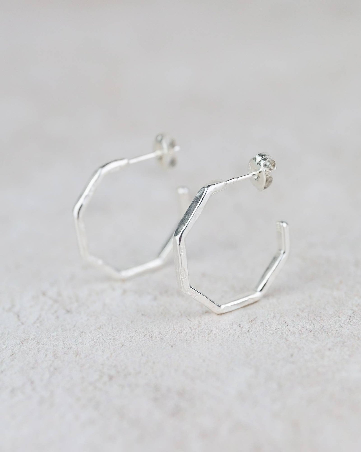 Silver hexagonal hoop earrings on a light gray background