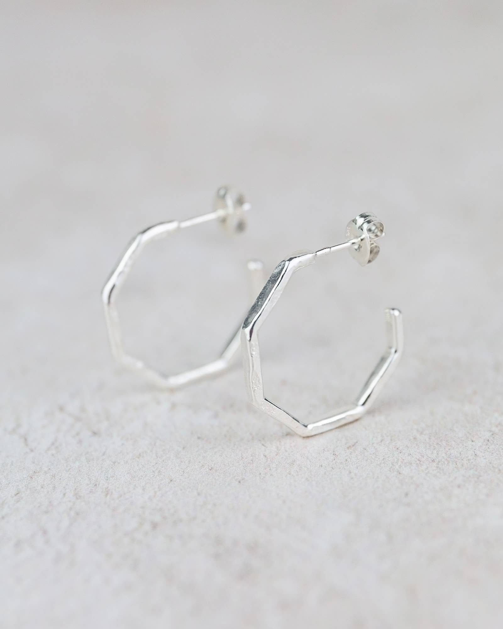 Silver hexagonal hoop earrings on a light gray background