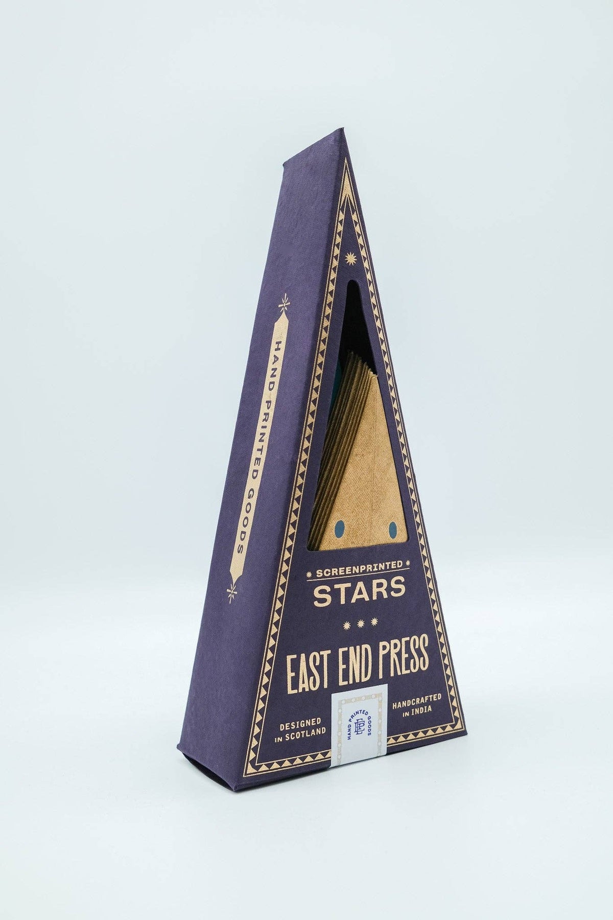 A triangular cardboard display box for the East End Press Stars Screenprinted Confectionery, featuring a deep purple exterior with gold decorative borders and text, and a clear window showing the gold-toned confectionery products inside, set against a light gray background.