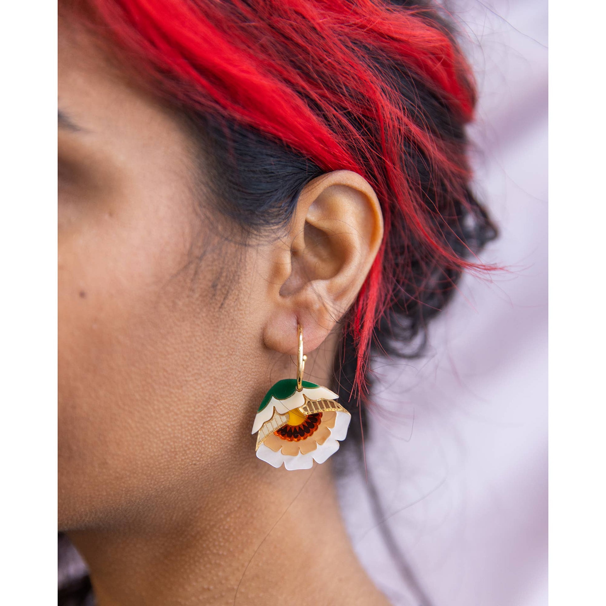 Close-up of a person wearing a floral earring with red hair.